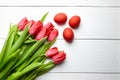 Easter Eggs and red flowers on white wooden table, top view. Painted chicken eggs and red tulip Royalty Free Stock Photo