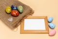 Easter eggs on a sackcloth bag and a frame on the beige background.