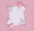 Easter eggs and white blossoms around blank note paper, on a pink background. Flat lay with copy space