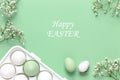 Easter eggs in a white holder and spring flowers on a green background. Copy space