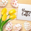 Easter eggs with yellow tulips flower and paper on the texture wooden background