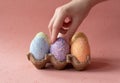 Easter eggs in brown box of eggs, hand on egg, beautiful pink background