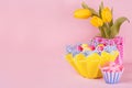 Easter festive background - yellow, blue, red eggs in yellow basket, tulips, cupcake on pastel pink background with copy space. Royalty Free Stock Photo