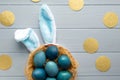 Easter flat lay with blue eggs in the basket and funny bunny ears on light blue wooden background with golden circles