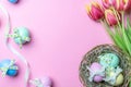 Easter flower. Colorful egg with tape ribbon, spring tulips, feathers on pastel pink background in Happy Easter decoration. Royalty Free Stock Photo