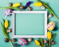 Easter Frame of beautiful yellow tulips, decorated eggs and beads on turquoise background Royalty Free Stock Photo