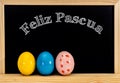 Easter frame with painted eggs and chalkboard. Happy Easter in white chalk. Happy Easter in spanish : feliz Pascua