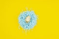 Easter gold chicken egg in a nest made of packing filler isolated on a yellow background. Top view Royalty Free Stock Photo
