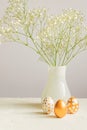 Easter golden eggs and bouquet of gypsophila flowers on the gray wall background. Festive cozy still life for holiday. Interior Royalty Free Stock Photo