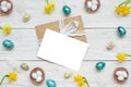 Easter greeting card in frame made of spring yellow Narcissus flowers and easter colorful eggs on white wooden