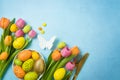 Easter holiday celebration concept with easter eggs gold flatware and tulip flowers on blue background. Top view, flat lay