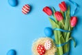 Easter holiday composition with colored eggs, ribbons and red tulip flowers on blue