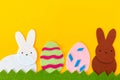 Easter holiday concept. Cut out of felt applications of two eggs and white and brown rabbits on the grass. Yellow background. Copy Royalty Free Stock Photo