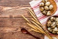 Quail eggs in a wooden bowls and plates on a rustic table linen with ears of wheat and wooden spoon on rustic background