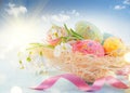 Easter holiday scene background. Traditional colorful eggs and spring flowers in the nest over blue sky Royalty Free Stock Photo