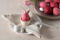 Easter holiday table setting, pink colored egg in cup with bunny ears, on plate with napkin, spoon and candies, on