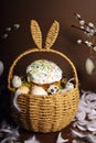 Easter holidays, cute basket with bunny ears on brown background. Easter cakes with colored sprinkles, colored golden eggs, and