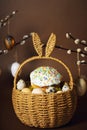 Easter holidays, cute basket with bunny ears on brown background. Easter cakes with colored sprinkles, colored golden eggs, and
