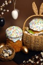 Easter holidays, cute basket with bunny ears on brown background. Easter cakes with colored sprinkles, colored golden eggs, and