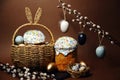 Easter holidays, cute basket with bunny ears on brown background. Easter cakes with colored sprinkles, colored golden eggs, and