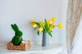 Easter home decor. Easter bunny rabbit statuette in straw basket with colored eggs, fresh spring tulips and daffodils Royalty Free Stock Photo