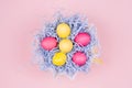 Easter home decor - homemade painted eggs in pastel blue nest on light pink background, top view.