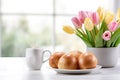 Easter hot buns with aromatic morning coffee in a modern kitchen. There is a vase with fresh tulips on the table