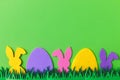Easter hunt concept. Colorful Easter bunnies and eggs in grass on green background, top view with space for text. Happy Easter! Royalty Free Stock Photo
