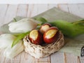 Easter painted eggs in a natural basket with white tulips.Wooden white background