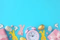 Flat lay photo of color eggs, cute rabbits, gift boxes and pink alarm clock on pastel blue background