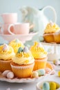 Easter pastry lemon cupcakes with yellow buttercream frosting decorated with sprinkles and chocolate eggs. Festive table setting Royalty Free Stock Photo