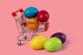 Easter postcard .Shopping cart with multi-colored eggs on a pink background .