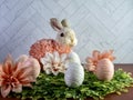 Easter rabbit bunny sitting on a bed of green leaves with peach dahlia flower blooms and string decorated white and peach Easter