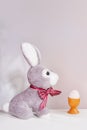 Easter rabbit toy and a cheerful egg in a nest on a white gray background Royalty Free Stock Photo
