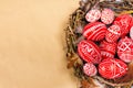 Easter red eggs with folk white pattern inside bird nest on sheet of paper background. Top view. Ukrainian traditional eggs