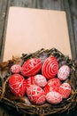 Easter red eggs with folk white pattern inside bird nest on sheet of paper on rustic wood background. Ukrainian traditional eggs