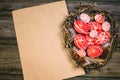 Easter red eggs with white pattern inside bird nest on right side of old sheet of paper on wood board. Top view Royalty Free Stock Photo