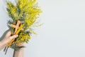 Womans hands hold wooden crucifixion, mimosa sprig and copy space