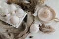 Easter rustic still life. Easter natural eggs in tray, feathers, willow branches, nest on burlap on white wooden table. Simple