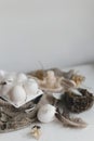 Easter rustic still life. Easter natural eggs in tray, feathers, willow branches, nest on burlap on white wooden table. Simple