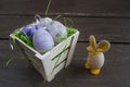 Easter small basket with colored eggs and a small egg rabbit on grey wooden board. Royalty Free Stock Photo