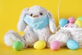 Easter bunny in mask and colored eggs in basket on yellow background. Ester holiday during coronavirus concept