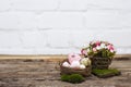 Easter table decoration with multi-coloured eggs in nest, basket with decorative flowers and moss on wooden table and white brick