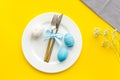 Easter table decoration. Plate, cutlery, painted eggs and dry white flowers, tablecloth on yellow background top view Royalty Free Stock Photo