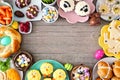 Easter table scene with a selection of breads, desserts and treats, top view frame over a wood background