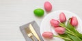 Easter table setting. Egg pastel color and pink tulip and gold cutlery on white wood, overhead