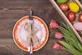 Easter table setting with empty orange plate and cutlery and multicolored eggs in a box on a wooden table. Holidays background Royalty Free Stock Photo