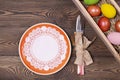 Easter table setting with empty orange plate and cutlery and multicolored eggs in a box on a wooden table. Holidays background Royalty Free Stock Photo