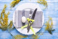 Easter table setting. White eggs, napkin on a plate, mimosa flowers, fork, knife on a blue wooden table Royalty Free Stock Photo