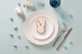 Easter table setting with white plate, glazed cookies and white bunny on blue .